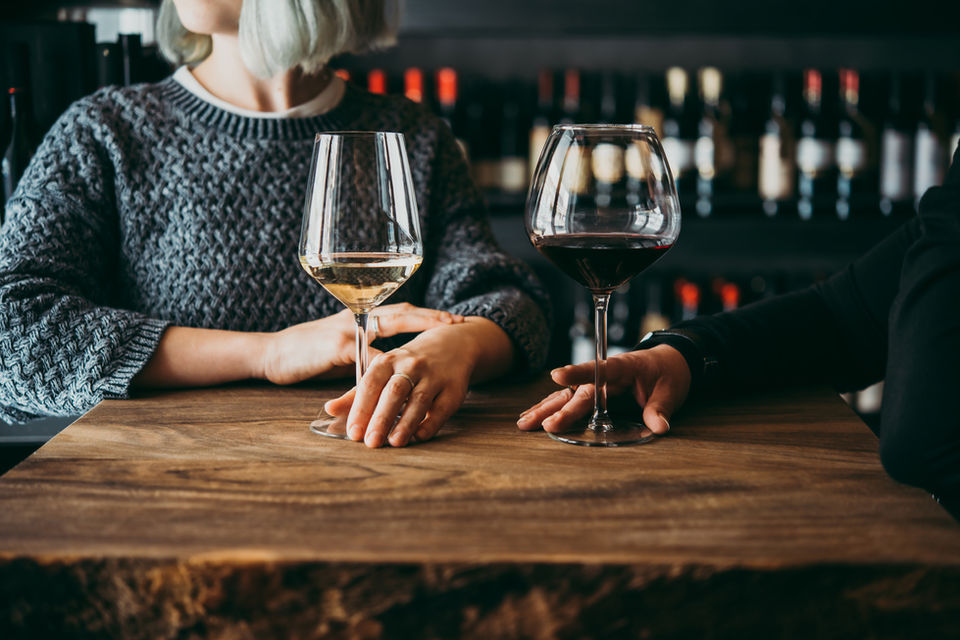 Cropped image of couple with wine glasses at wooden table.