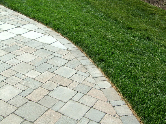 Close up view of clean grey block paving stones laid in a uniform pattern next to a lush green domestic lawn