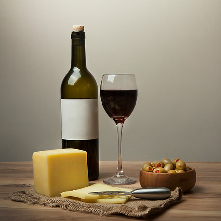 A bottle of red wine, a filled wine glass, a block and slices of cheese