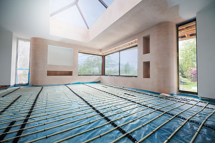 Interior view of a room under construction featuring in-floor heating pipes laid on a protective blue plastic barrier