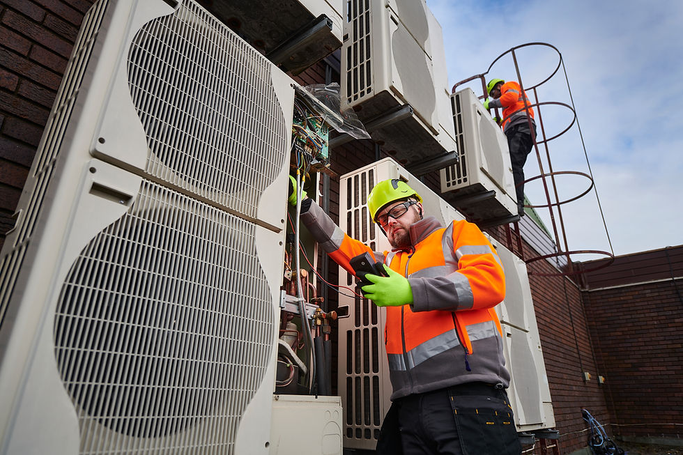 An HVAC technician in a hard hat and safety vest checks a phone while servicing a large outdoor AC