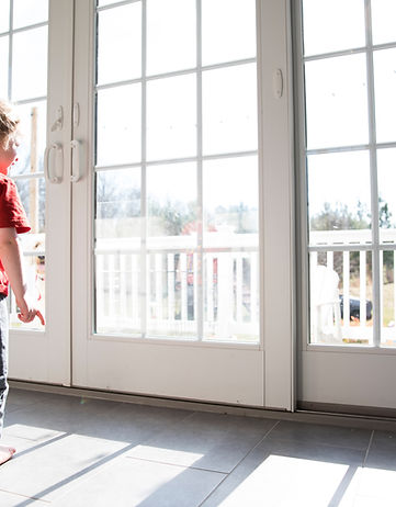 Toddler Boy Looks Out Large Sliding Glass Door at Dog on Deck