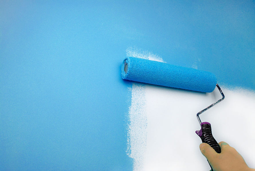 Hand holding a paint roller applies bright blue paint on a white wall