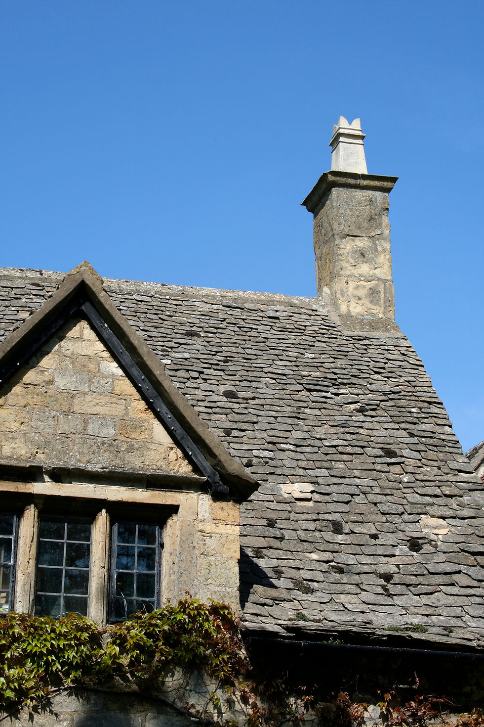 Stone gable end wall with a stone tile roof and chimney against a blue sky