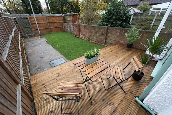 A general exterior view of a back garden patio area with wood decking, potted plants, Drag