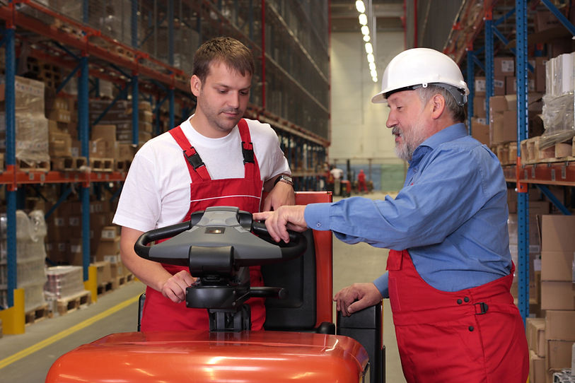 A senior worker teaching his junior the operation of a fork lift vehicle in a factory