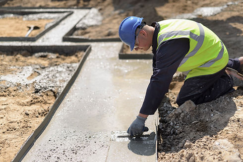 A construction worker in a blue helmet and yellow vest smooths wet concrete on a building site, focusing intently