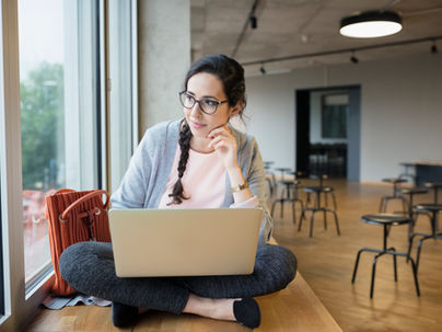 Woman sitting on a table looking out of a window while working on her laptop