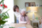 A woman gently combs the hair of an elderly woman seated at a table