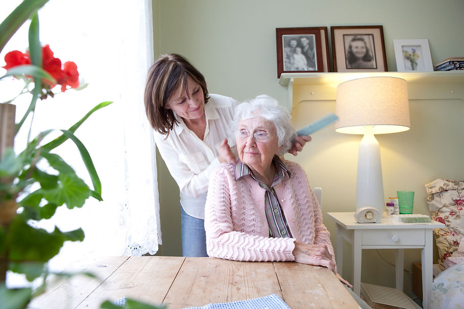 A woman gently combs the hair of an elderly woman seated at a table