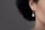 Close-up of a woman's ear adorned with an elegant teardrop diamond earring against a soft grey background