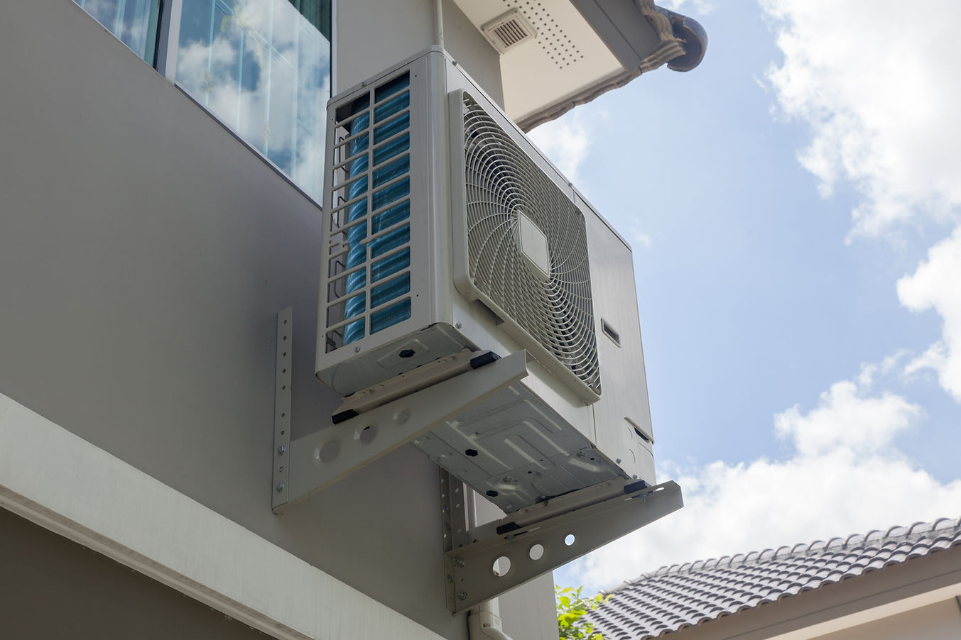 Wall-mounted air conditioning unit outside a building with a clear blue sky in the background