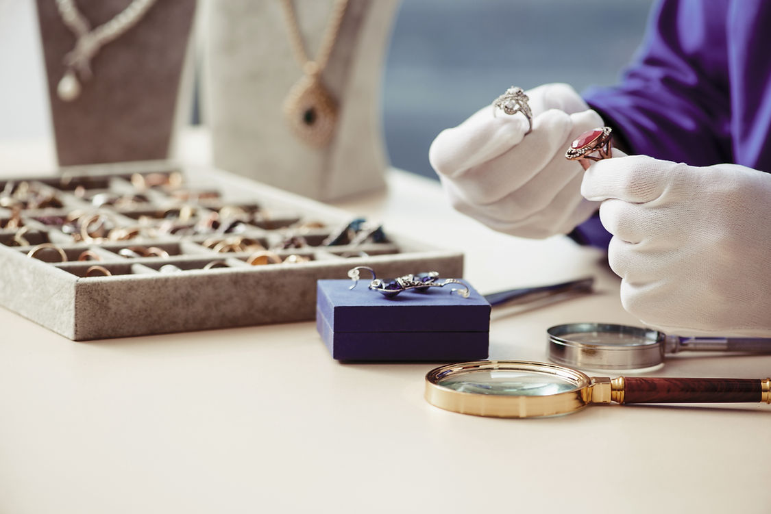 A person wearing white gloves examines rings, with a jewelry box and scattered tools