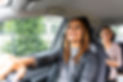 Two women are sitting in a car, one is driving and the other one is sitting in the backsea