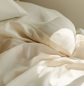 A close up of a bed showing a duvet and pillow in cream linen with sunlight and shadow 
