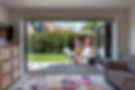 Open patio doors reveal a sunny garden with wicker furniture
