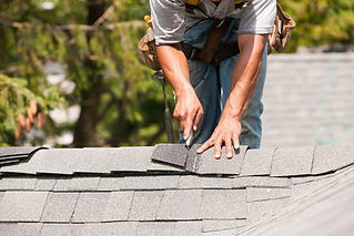 Carpenter cutting shingles on roof peak