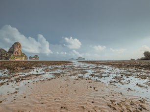 Rocky tidal flat with limestone cliffs and islets under a cloudy blue sky, calm and empty at low tide