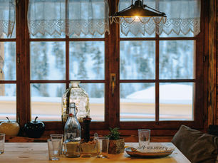 Cozy dining area with vintage overhead lamp, cafe curtains and rustic window frames and hardware with formable and cozy bench with pillows.
