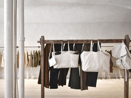 Neutral colored clothes and white bags hanging on wooden fixture in retail shop