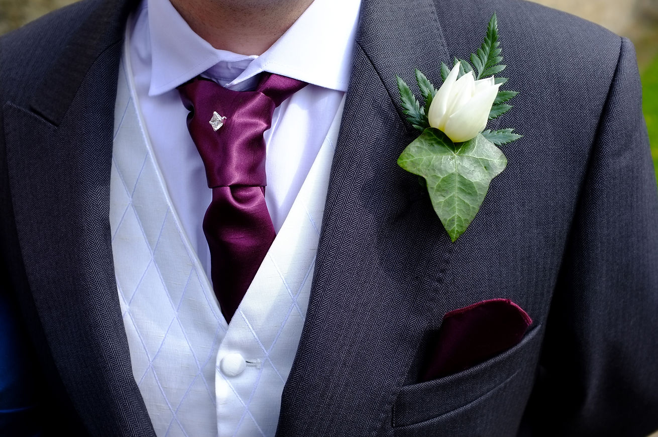 A person in a grey suit with a purple tie and a white boutonnière