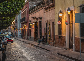 Photographe cadrant une ruelle pavée du village médiéval de Pérouges, avec maisons en pierre et lumière du matin filtrée à travers les volets anciens.