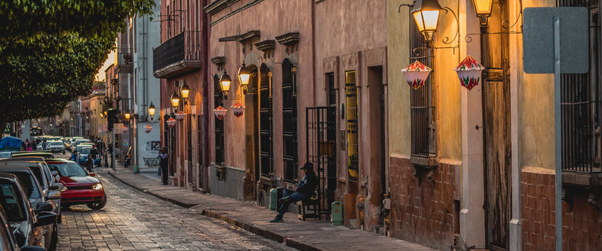 Photographe cadrant une ruelle pavée du village médiéval de Pérouges, avec maisons en pierre et lumière du matin filtrée à travers les volets anciens.