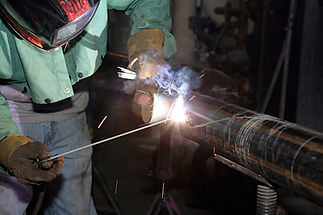 Close-up of a worker welding a large metal pipe in a workshop setting