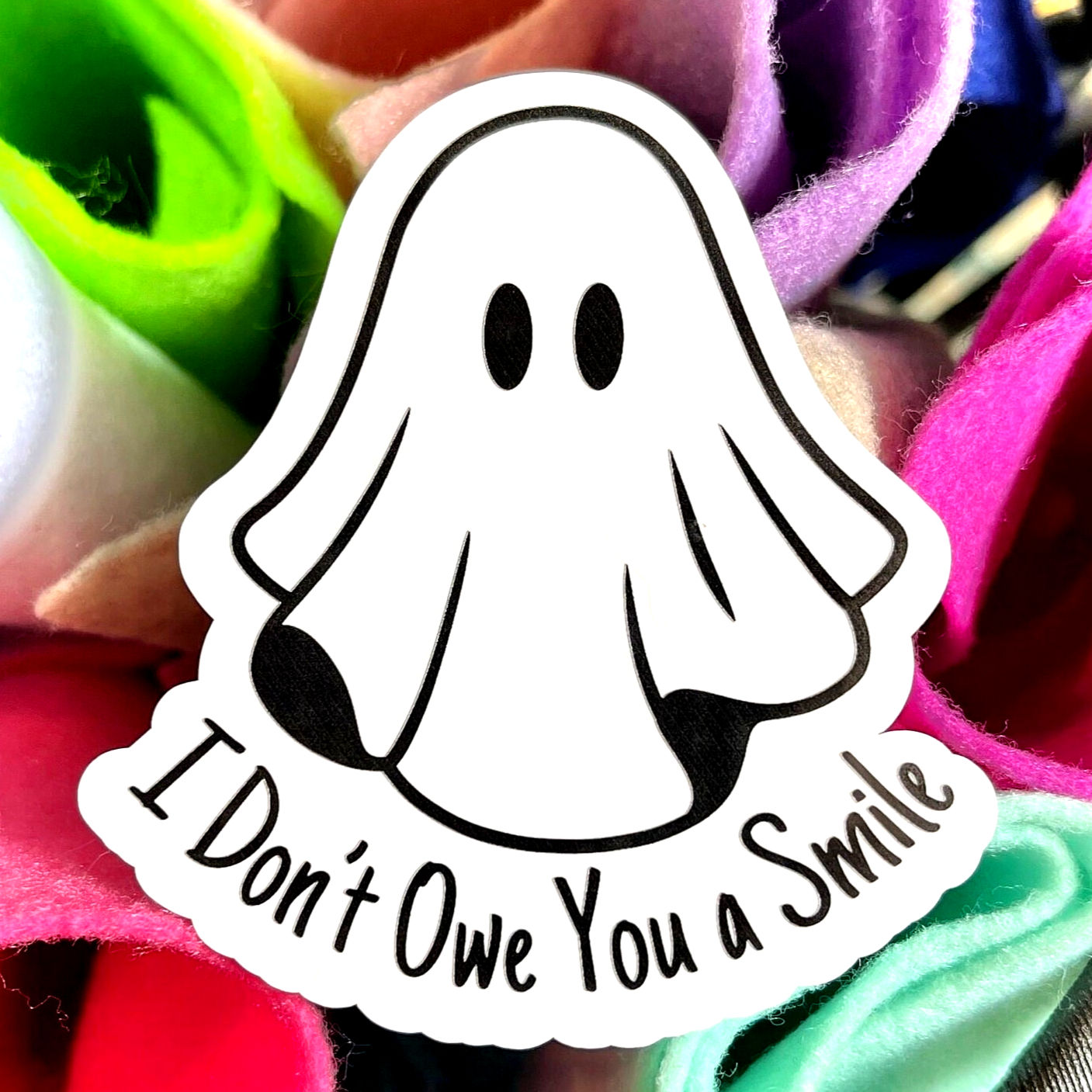 vinyl sticker of a cartoon ghost with no mouth and the phrase "I don't owe you a smile"