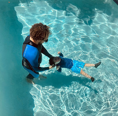 A swim instructor supports a preschool child floating on their back in a clear swimming pool during a private swim lesson, helping the child practice water safety and floating skills.