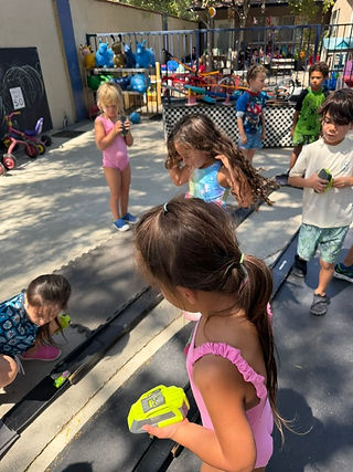 Children playing outdoors with toy cars and trucks during a group activity.