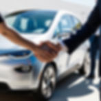 Two people stand in front of a used electric car and shake hands.