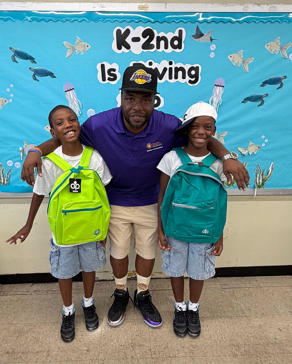 Mr. Keith stands in the middle with his arms around two middle school age boys who are wearing their backpacks in front of them.