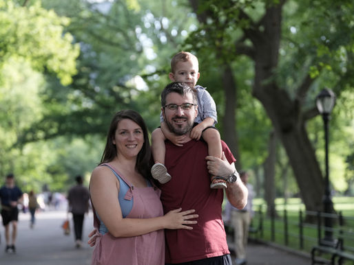 Anica, a client of the perinatal intensive outpatient program and Early Head Start, and her husband are standing with Luka on her husband's shoulders. They are in a park.