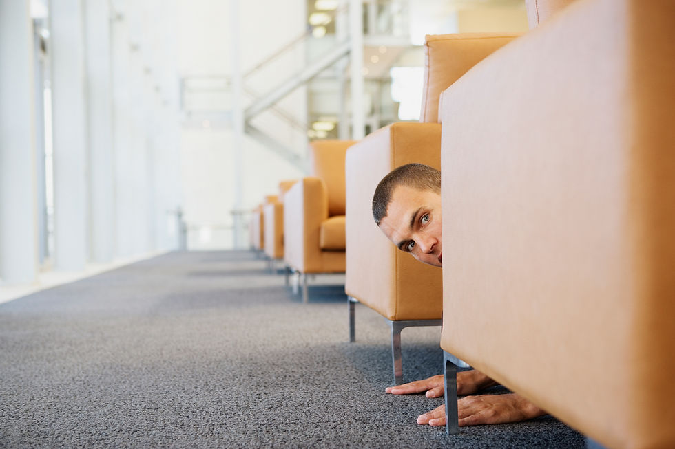 Ein Mann versteckt sich im Büro hinter einem Sessel, damit der Kunde ihn nicht sieht