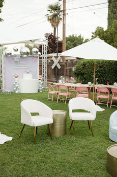 Outdoor event with white chairs and decorated dining area.