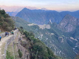 Turistas caminan por sendero montañoso con Machu Picchu al fondo y montañas. Extrema Aventura Por