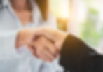 woman with white blouse shaking hands with someone with a black jacket sleeve