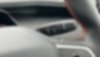 Close-up of a car's gear lever with labels R, N, D, P and cruise control icon. Black with orange stitching on steering wheel.