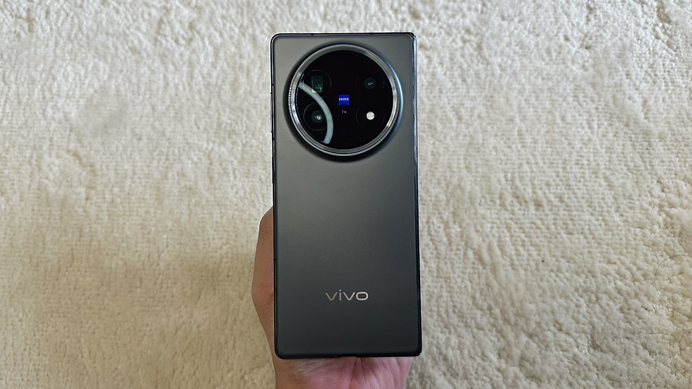 A hand holds a gray Vivo smartphone with a large circular camera module. The background is a textured beige surface.