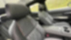 Luxury car interior with black leather seats featuring orange stitching. Raindrops on the window and greenery visible outside.