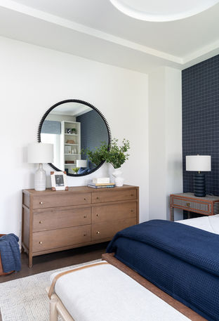 Boy's bedroom with wooden dresser, round mirror, lamp, picture frame, bed bench, a rug, striped nightstand, and a bed.