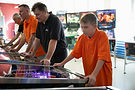 People playing pinball, arcade game. Orange shirts. Association with gaming. Pinball.