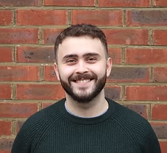 Smiling man in dark green sweater against brick wall