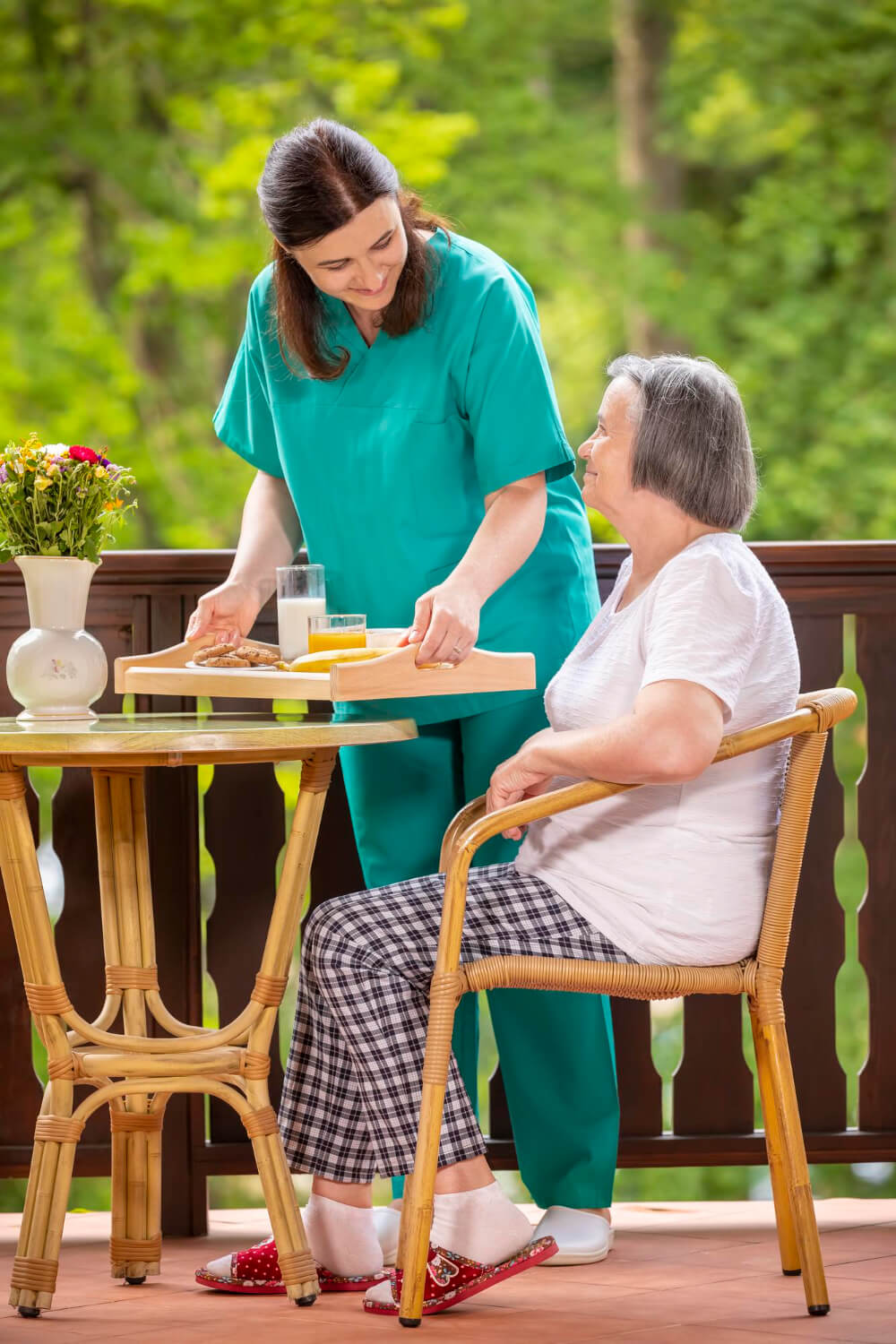 Caregiver serves breakfast to an elderly woman on a balcony, Seniors Paradise.