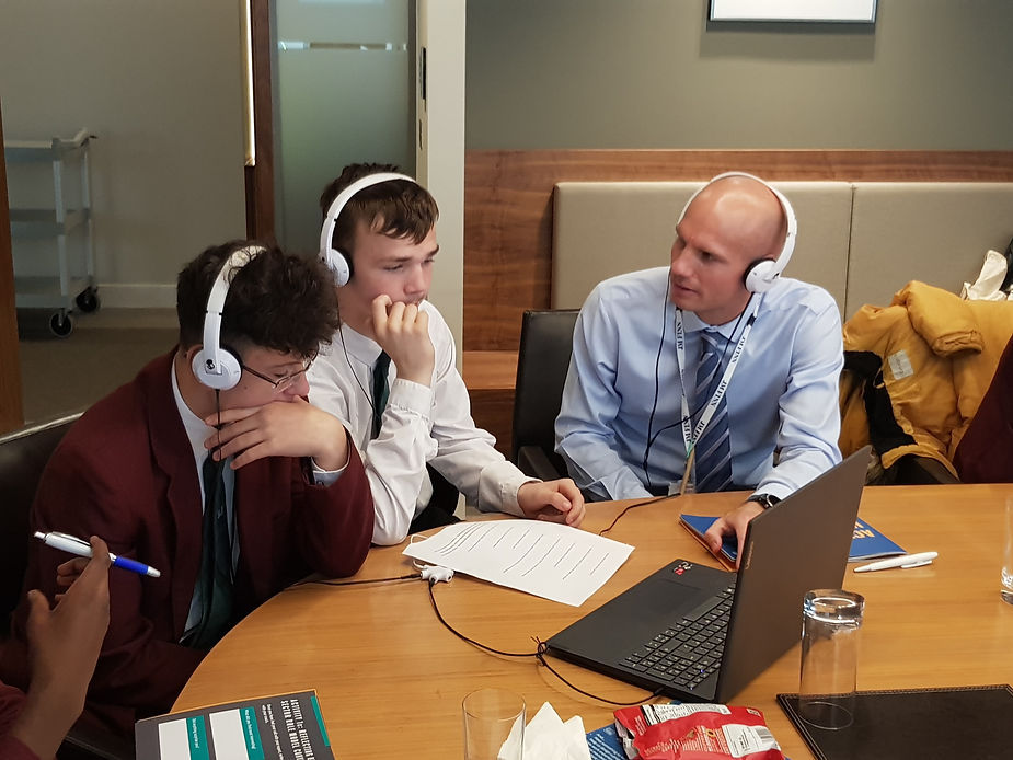 Three people wearing headphones at a table with a laptop in a meeting room.