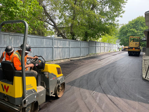Worker operating roller compacting asphalt on a road, a construction site scene.