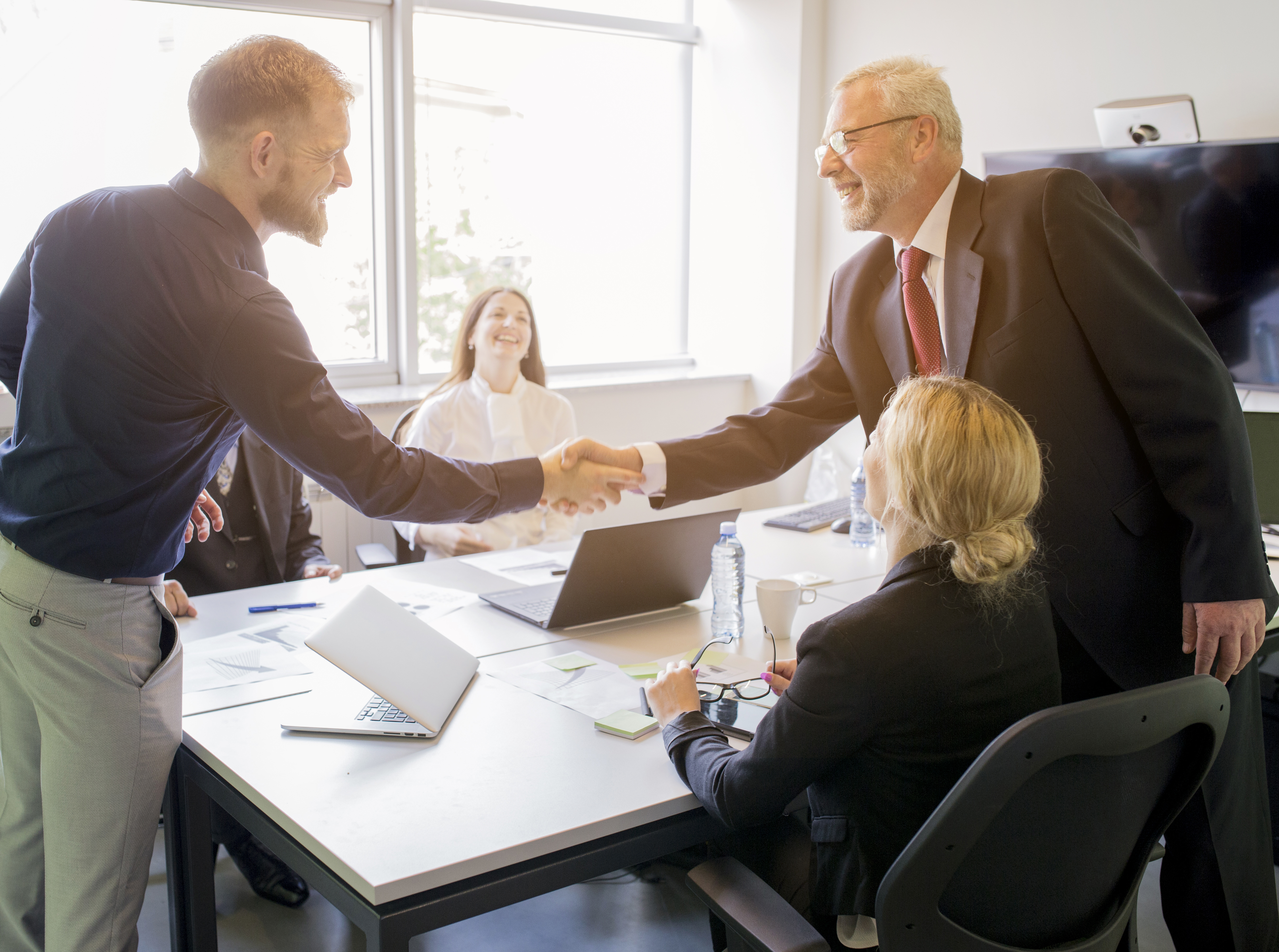 two-smiling-businessman-shaking-hands-together-board-meeting.jpg
