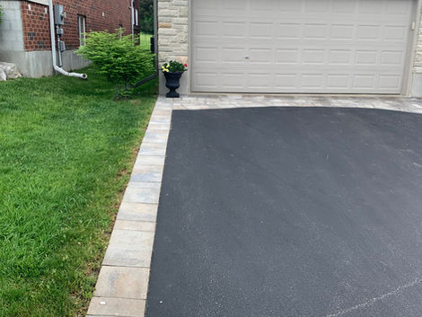 Asphalt driveway next to green grass and a garage door with house.