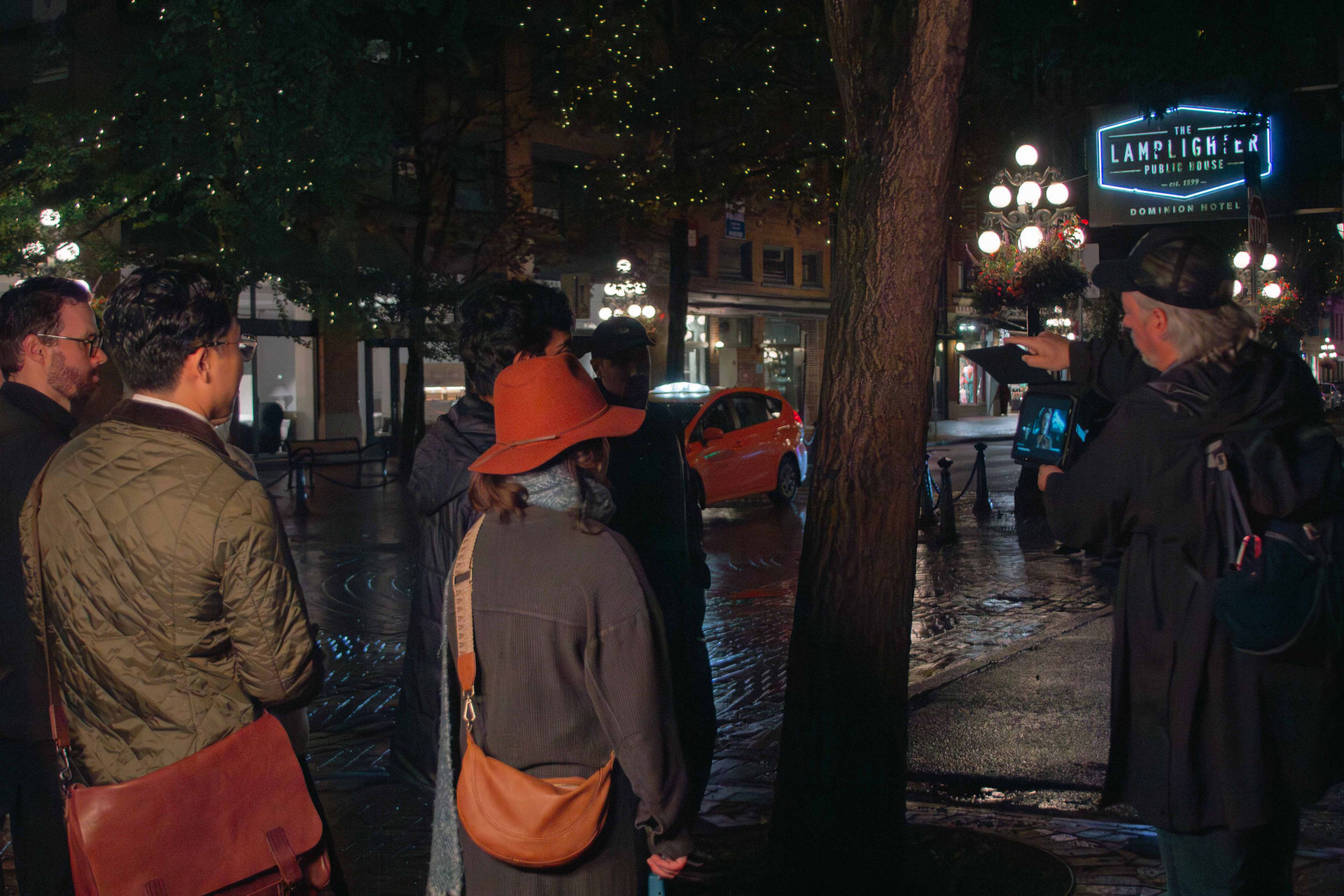 Group of people standing near a tree, Lamplighter sign in background.